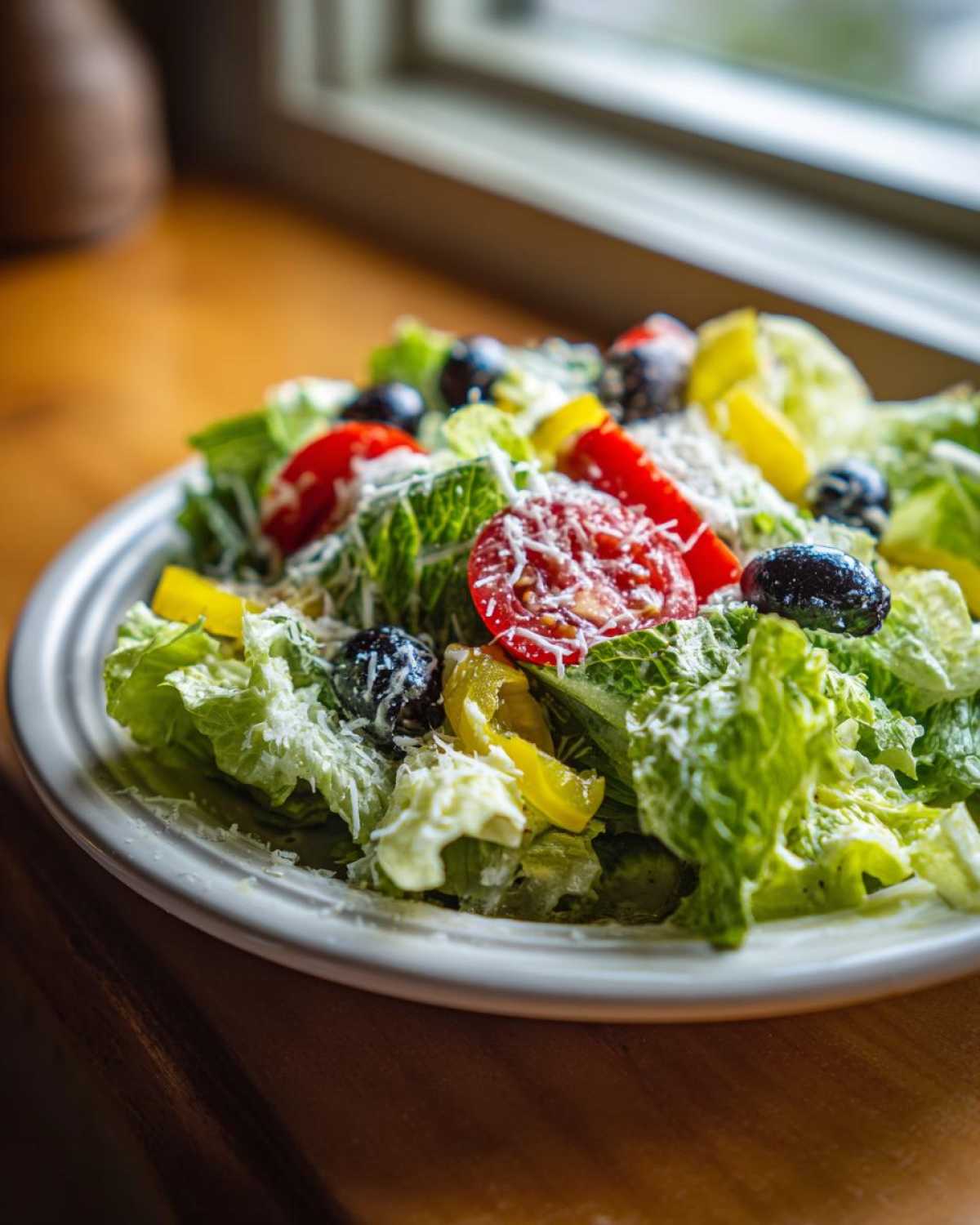 A vibrant plate of copycat Olive Garden salad featuring crisp lettuce, tomatoes, black olives, pepperoncini, and grated Parmesan cheese.