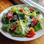 A fresh bowl of copycat Olive Garden salad featuring crisp lettuce, tomatoes, black olives, pepperoncini, and grated Parmesan cheese.