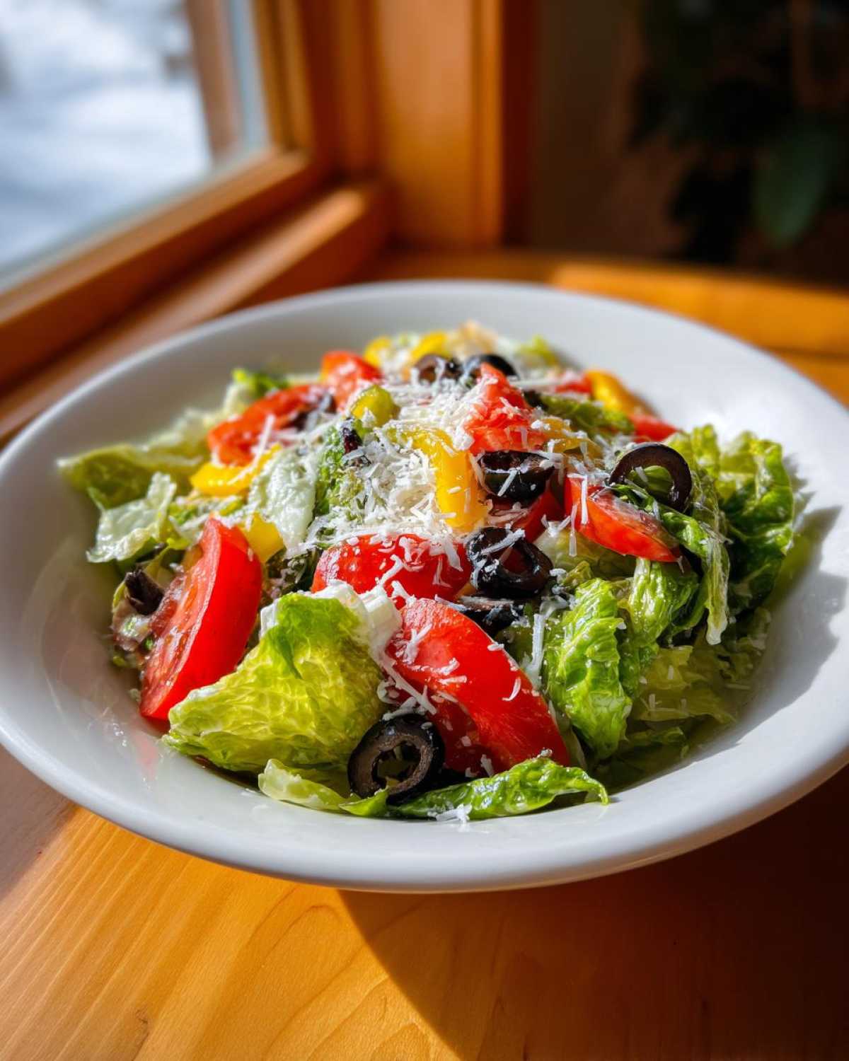 A vibrant bowl of copycat Olive Garden salad featuring crisp lettuce, tomatoes, olives, and grated cheese.