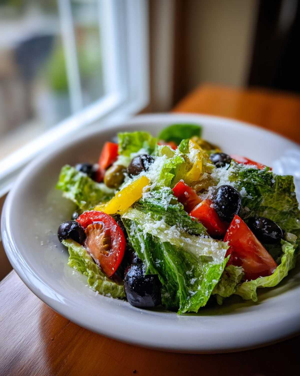 A close-up of a fresh copycat Olive Garden salad featuring crisp romaine lettuce, tomatoes, black olives, and grated Parmesan cheese.
