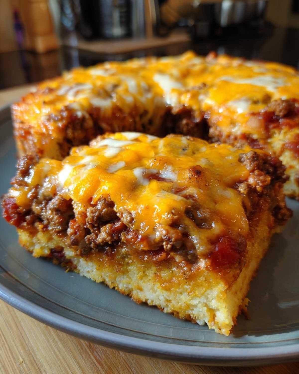 A close-up slice of cowboy cornbread casserole featuring a thick cornbread base topped with savory meat and melted cheddar cheese.