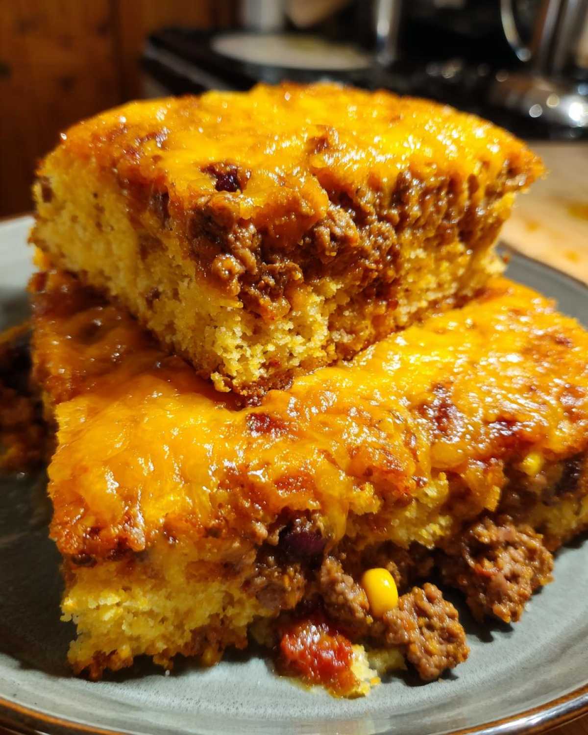 Two stacked squares of cowboy cornbread casserole featuring a thick layer of seasoned ground beef and melted cheddar cheese topping.