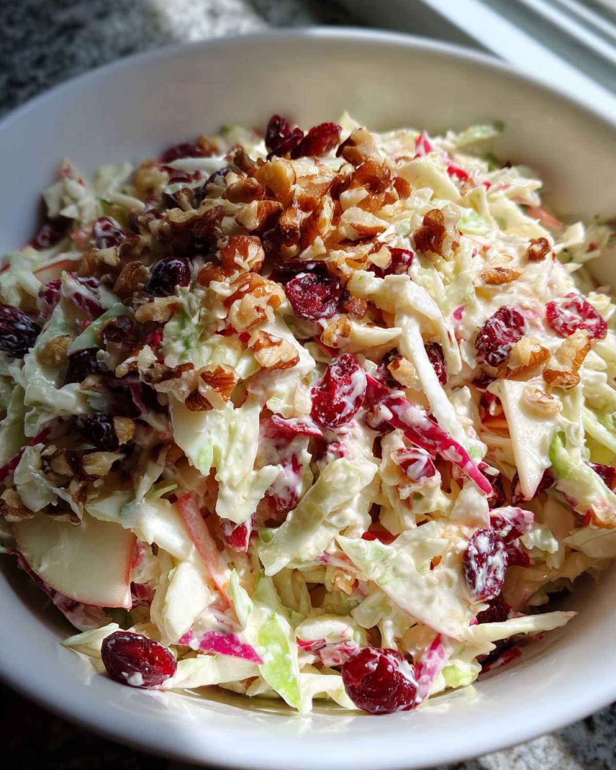 Close-up of creamy apple cranberry coleslaw topped generously with chopped walnuts and dried cranberries.