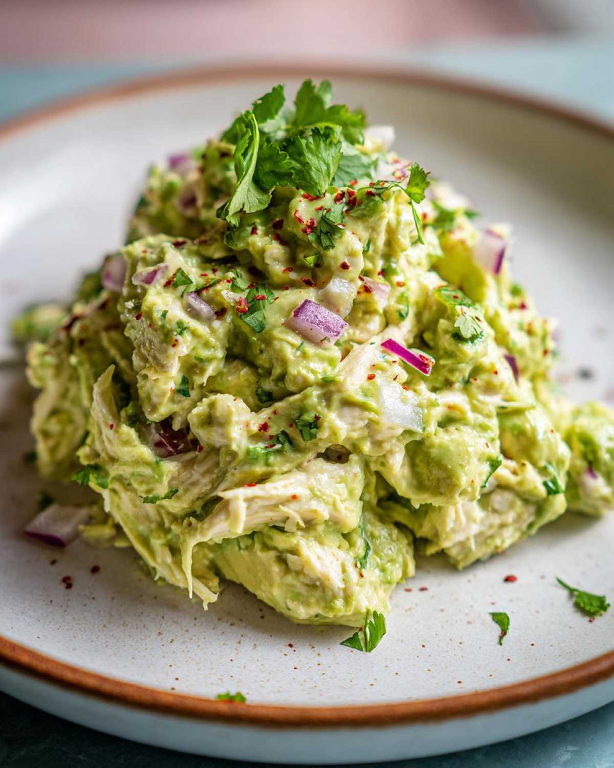 A mound of creamy avocado chicken salad mixed with red onion and topped with fresh cilantro.