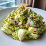 A close-up serving of creamy avocado egg salad featuring chunks of hard-boiled egg, diced red onion, and chives.