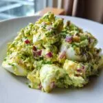 A close-up serving of creamy avocado egg salad featuring chunks of hard-boiled egg, diced red onion, and chives.