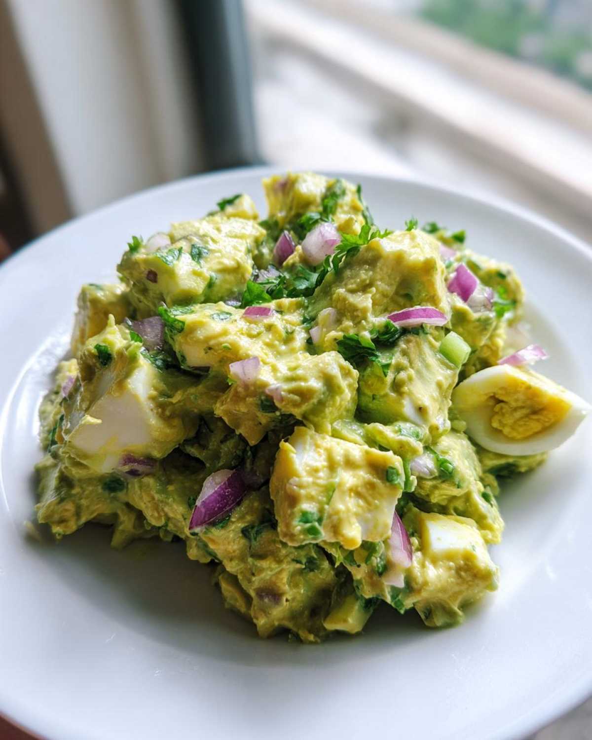 A close-up of creamy avocado egg salad mixed with chunks of hard-boiled egg and topped with diced red onion.