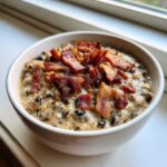 A white bowl filled with creamy black eyed peas mixed with spices and topped generously with crumbled, crispy bacon.