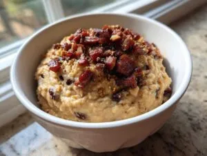 A white bowl filled with creamy black eyed peas mash, topped generously with crispy bacon bits.
