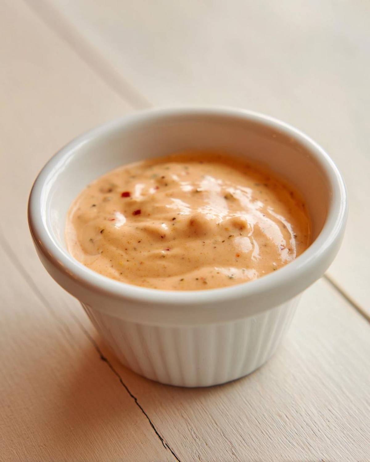 Close-up of creamy, orange-hued burger sauce speckled with spices in a small white ramekin.