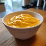 A close-up of thick, bright orange cottage cheese queso dip served in a small white bowl.
