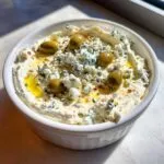 A creamy dirty martini dip topped with crumbled blue cheese, green olives, and olive oil.