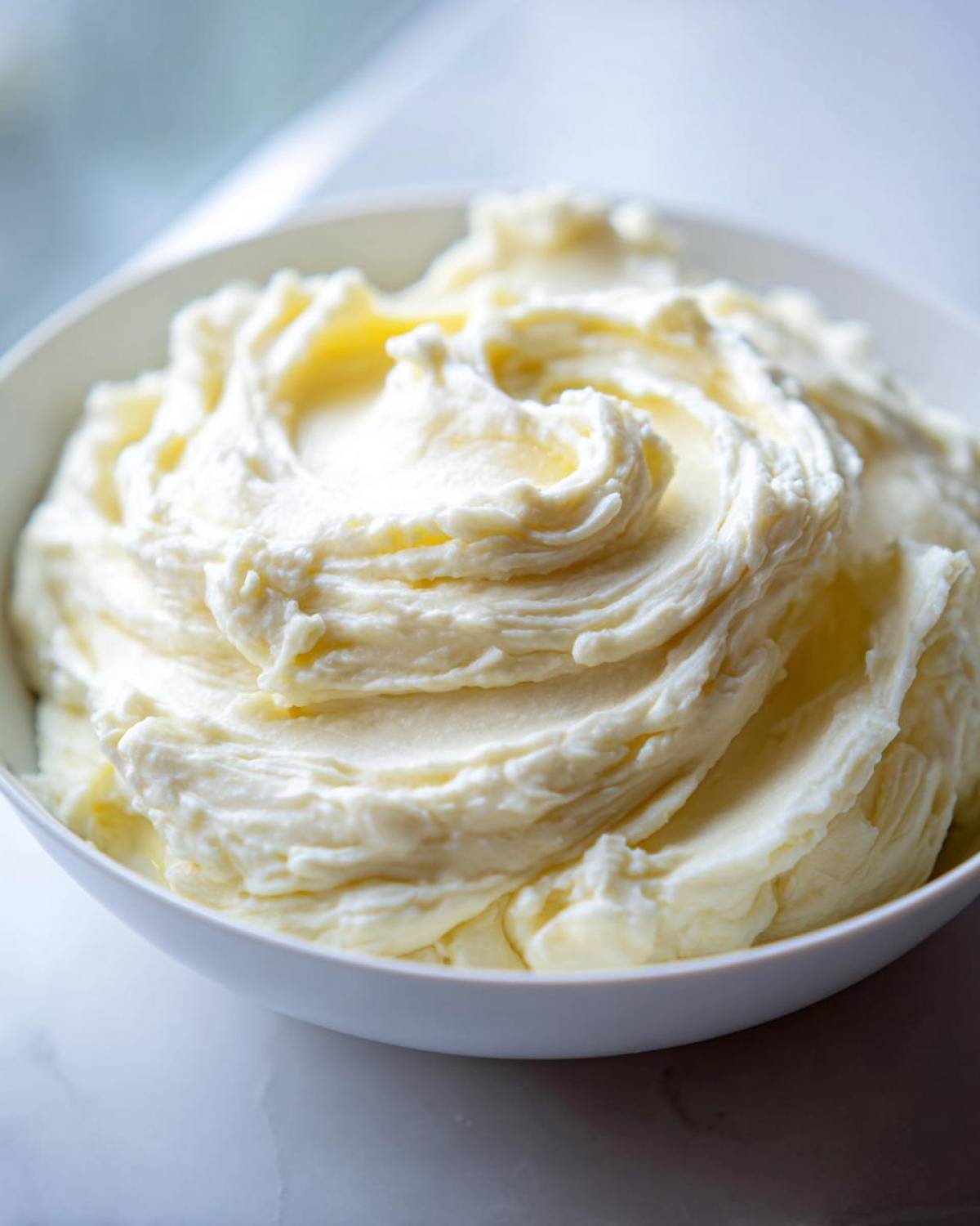 Close-up of ultra creamy garlic mashed potatoes swirled high in a white serving bowl.