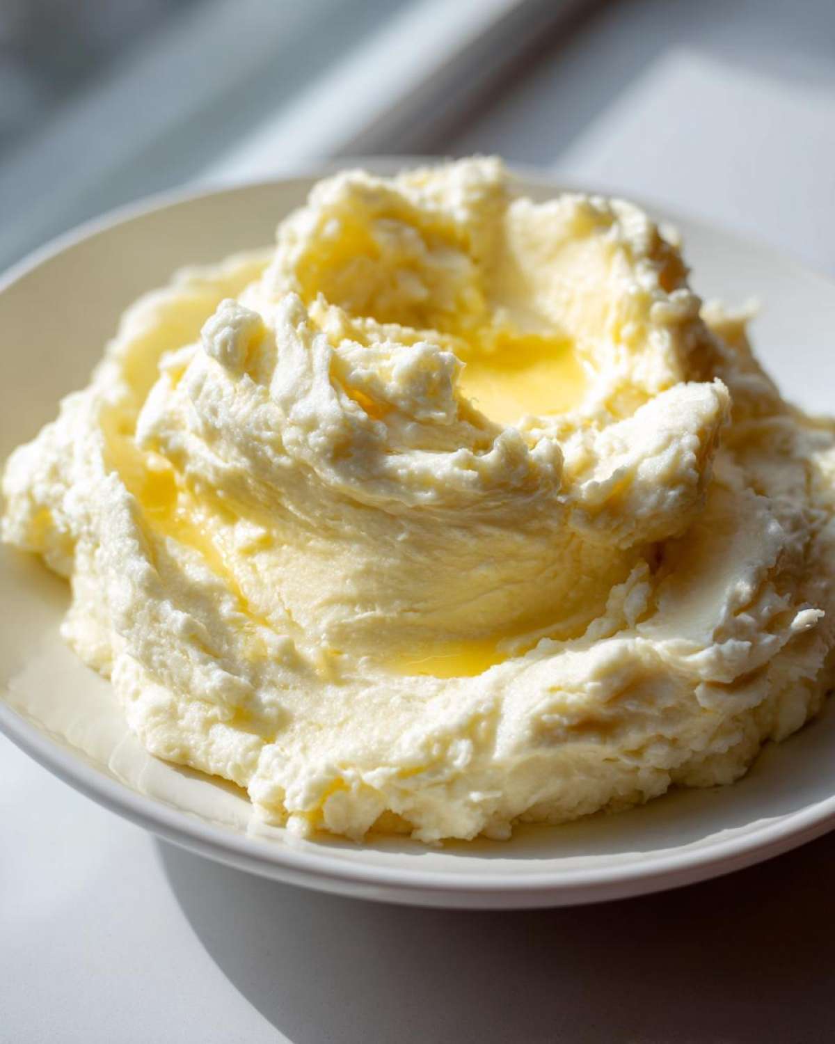 A close-up of ultra creamy garlic mashed potatoes served in a white bowl with a pool of melted butter on top.