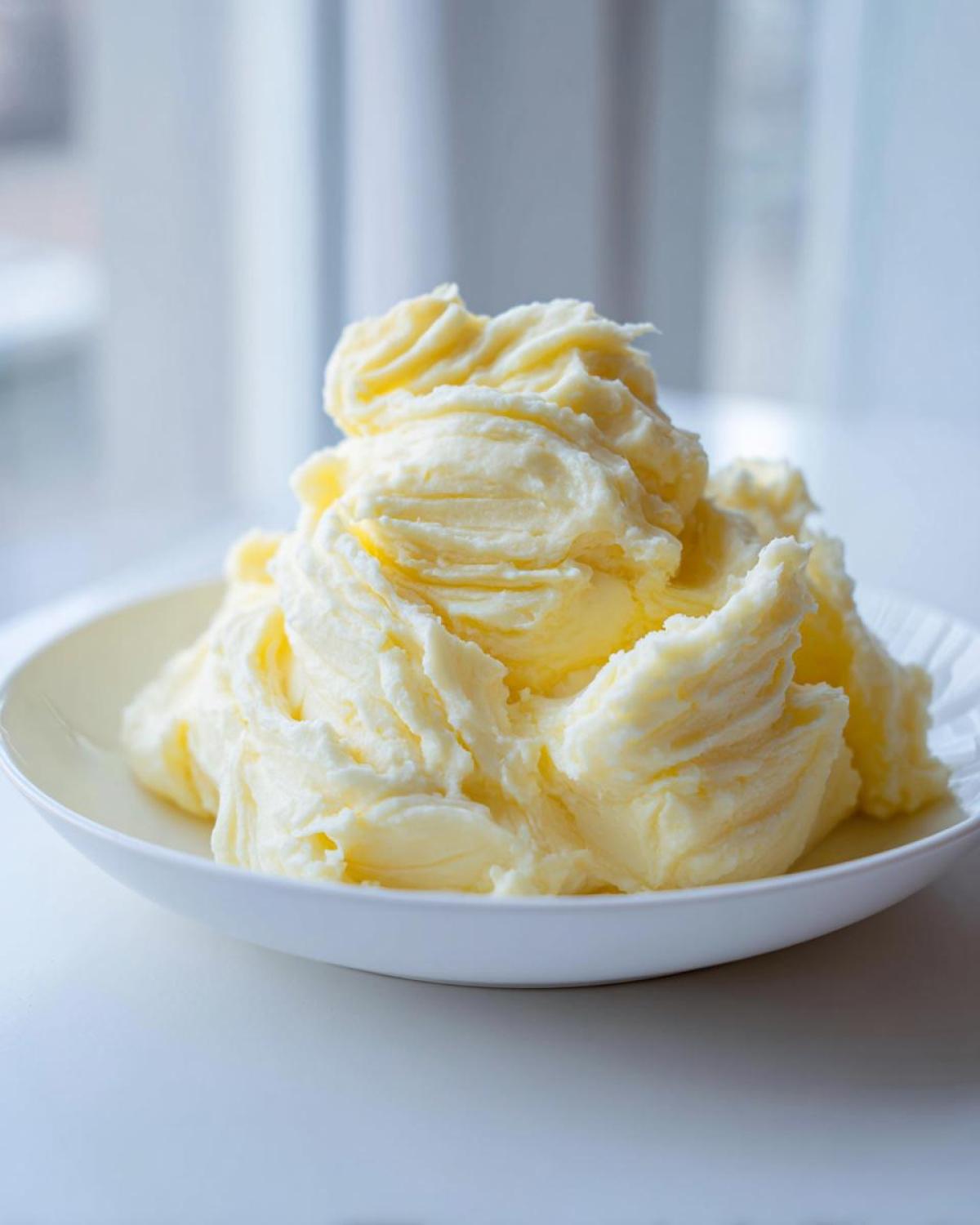 A large mound of ultra creamy garlic mashed potatoes swirled high in a white bowl.