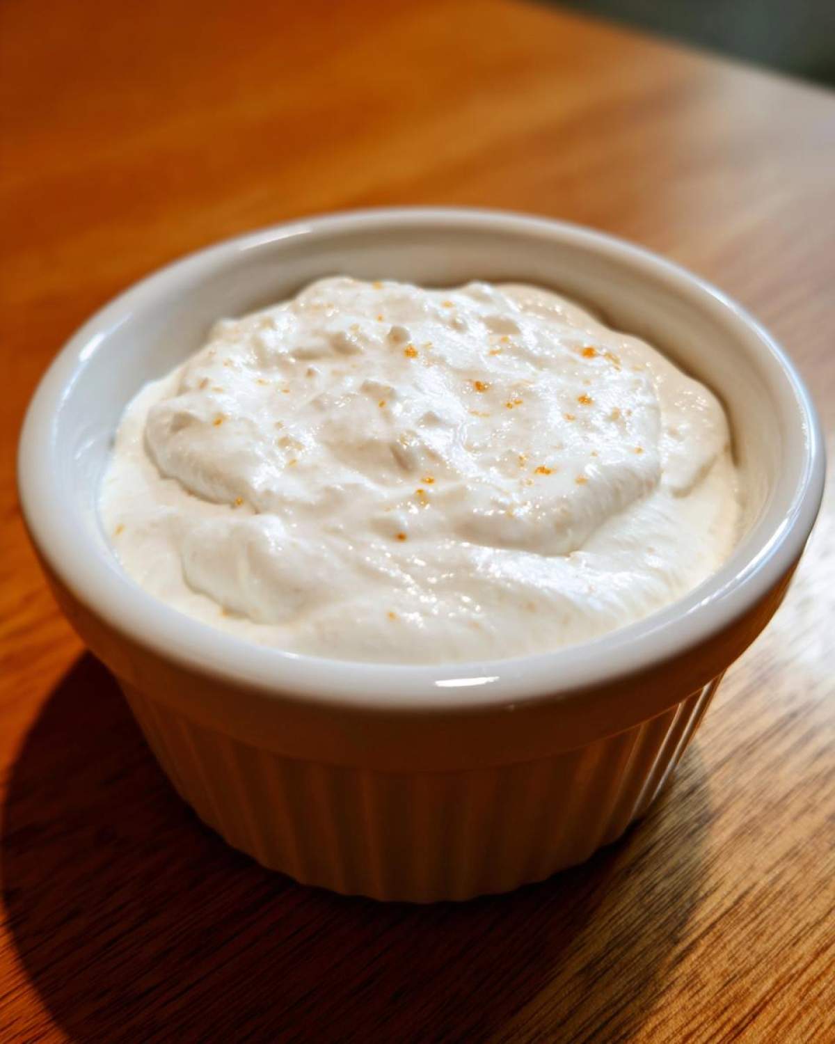 A close-up of thick, creamy garlic sauce sprinkled with orange zest in a small white ramekin.