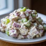 A close-up of creamy ham salad featuring diced pink ham, green celery, and black pepper on a light plate.