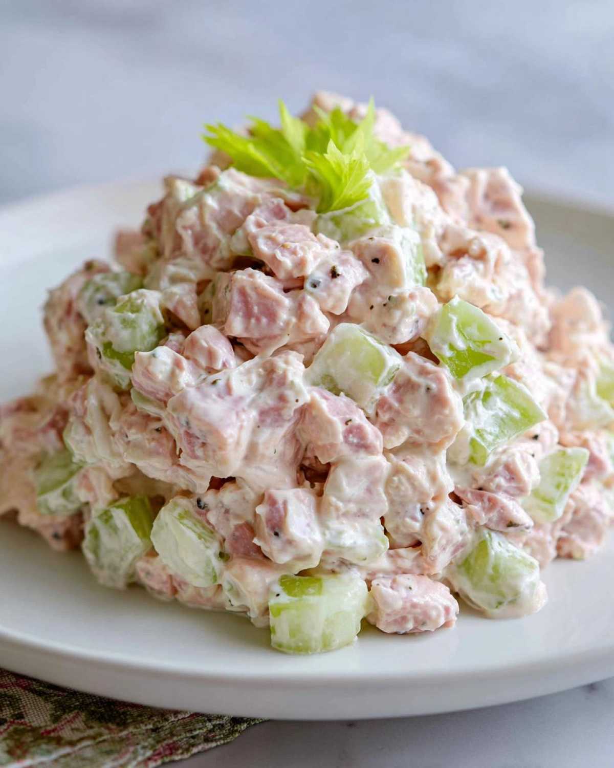 A mound of creamy ham salad mixed with chunks of celery, garnished with fresh celery leaves.