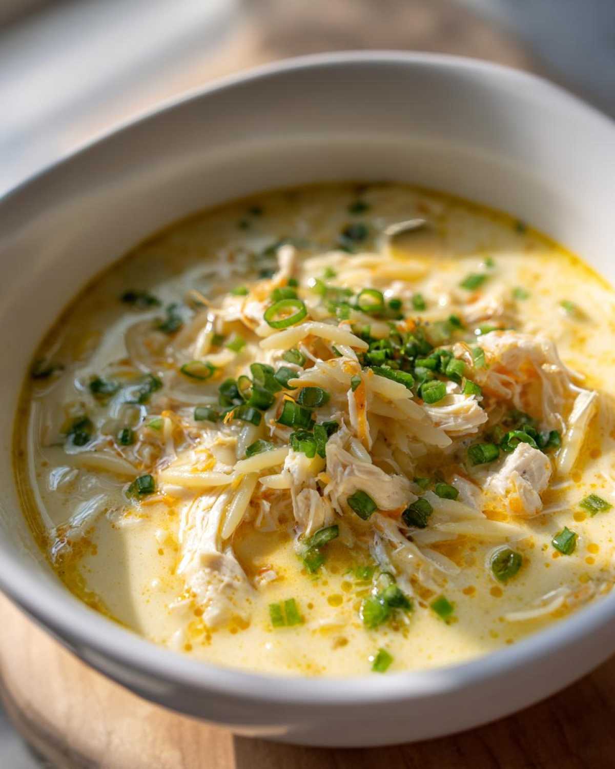 Close-up of creamy lemon chicken soup with shredded chicken, orzo pasta, and fresh green chives.