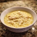 Close-up of a bowl of creamy lemon chicken soup featuring shredded chicken and orzo pasta.