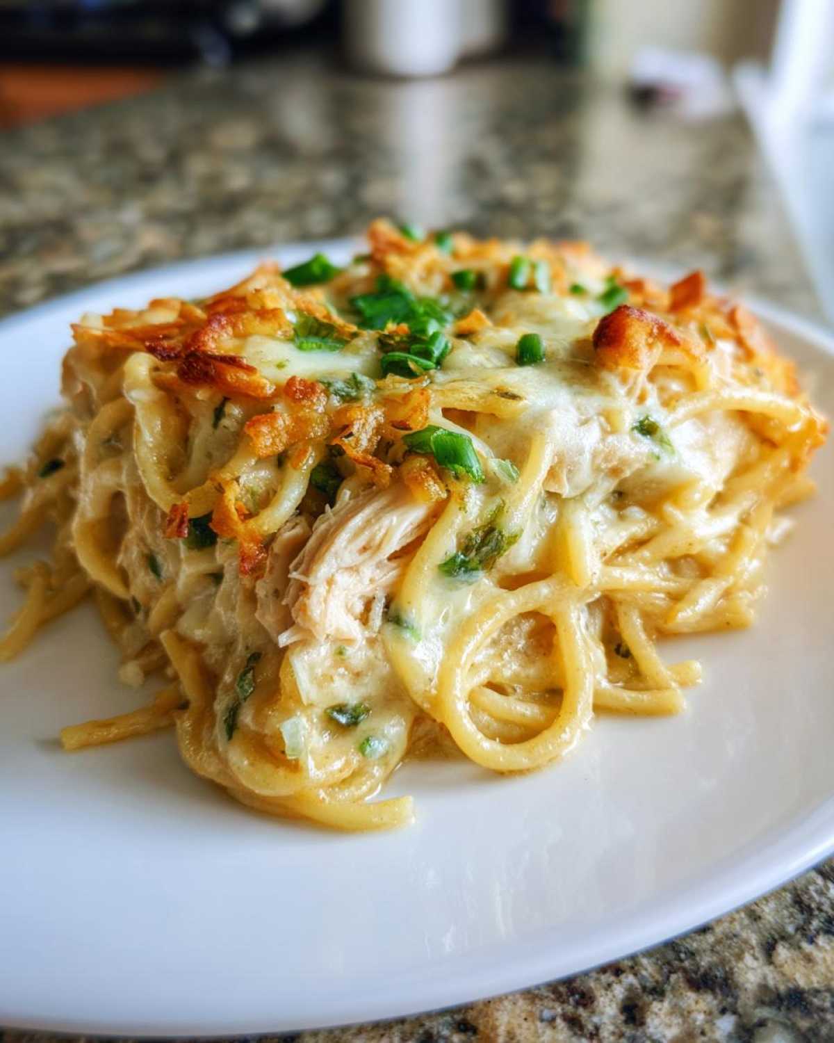 A close-up serving of creamy Monterey chicken spaghetti topped with melted cheese and green onions.