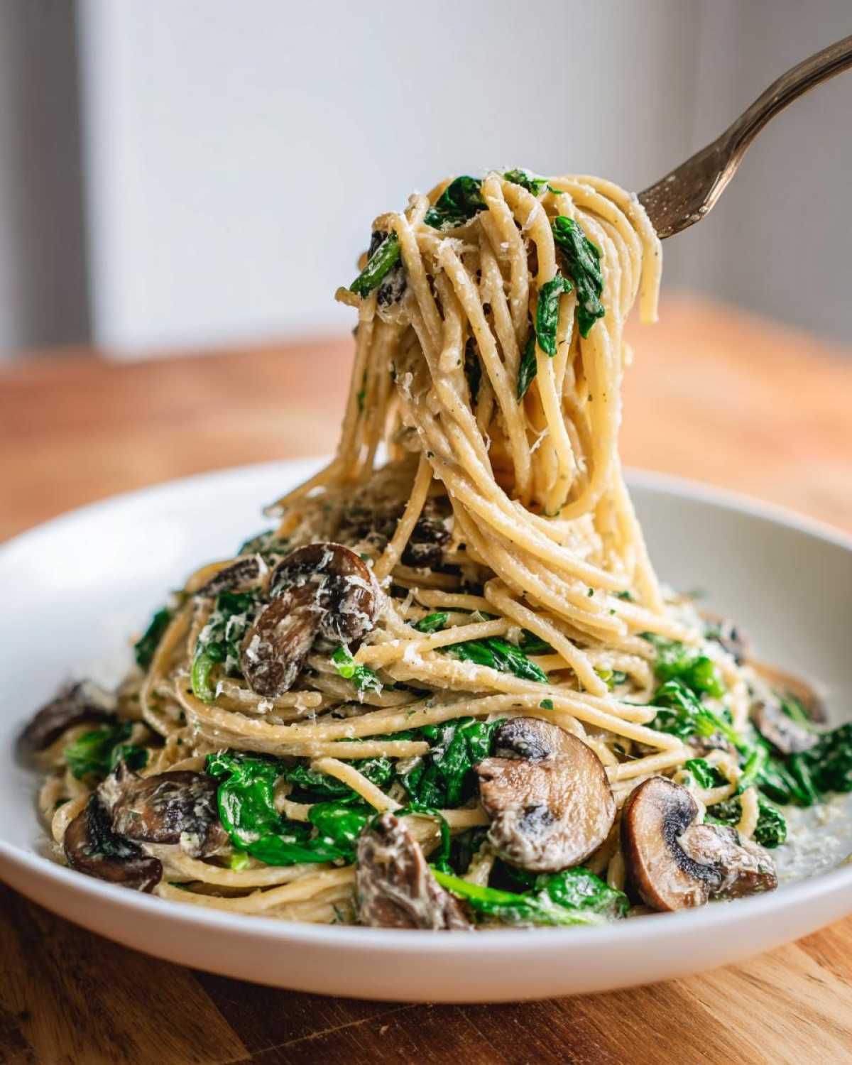 A fork lifts creamy mushroom pasta mixed with spinach from a white bowl.