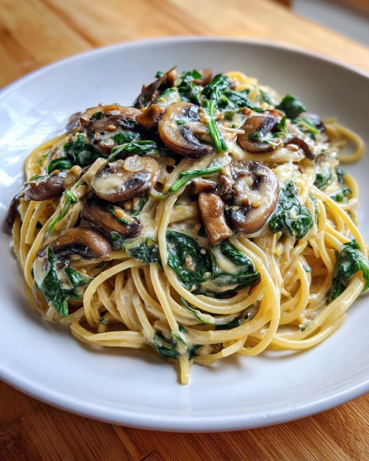 A close-up of creamy mushroom pasta tossed with wilted spinach, served in a white bowl.
