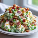 A large mound of creamy pea salad mixed with eggs and topped generously with crispy bacon bits.