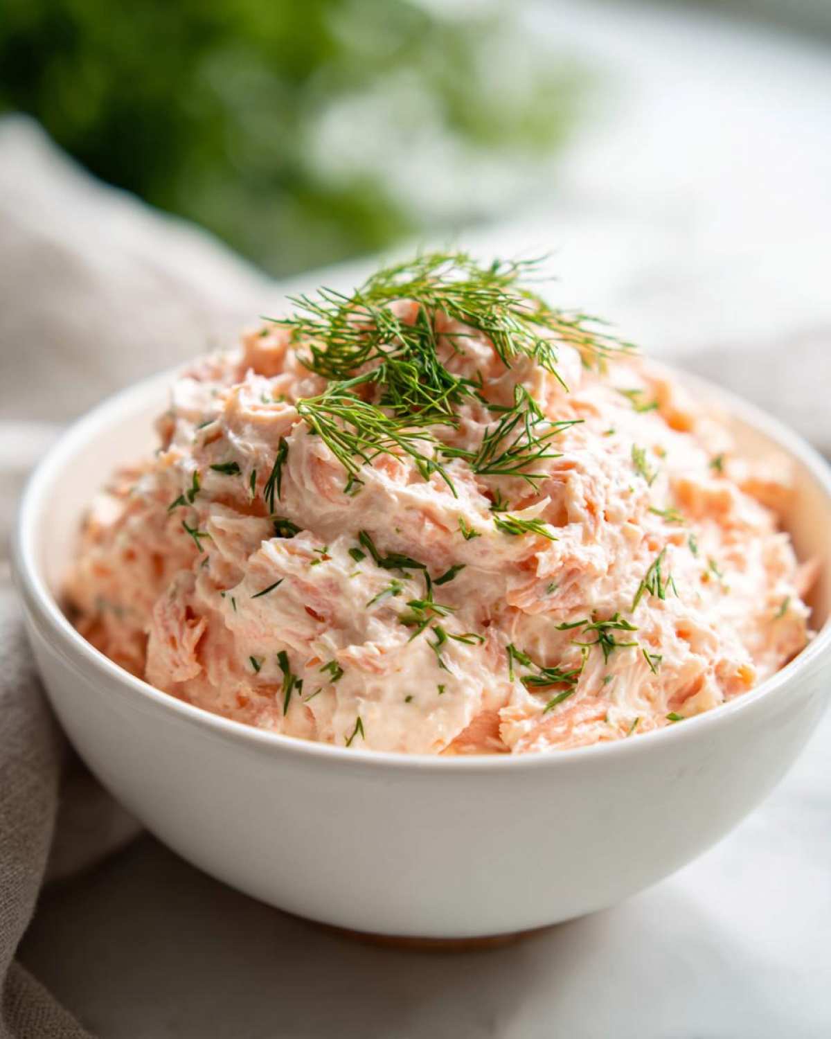 A close-up of creamy salmon dip mixed with herbs, topped generously with fresh dill sprigs.