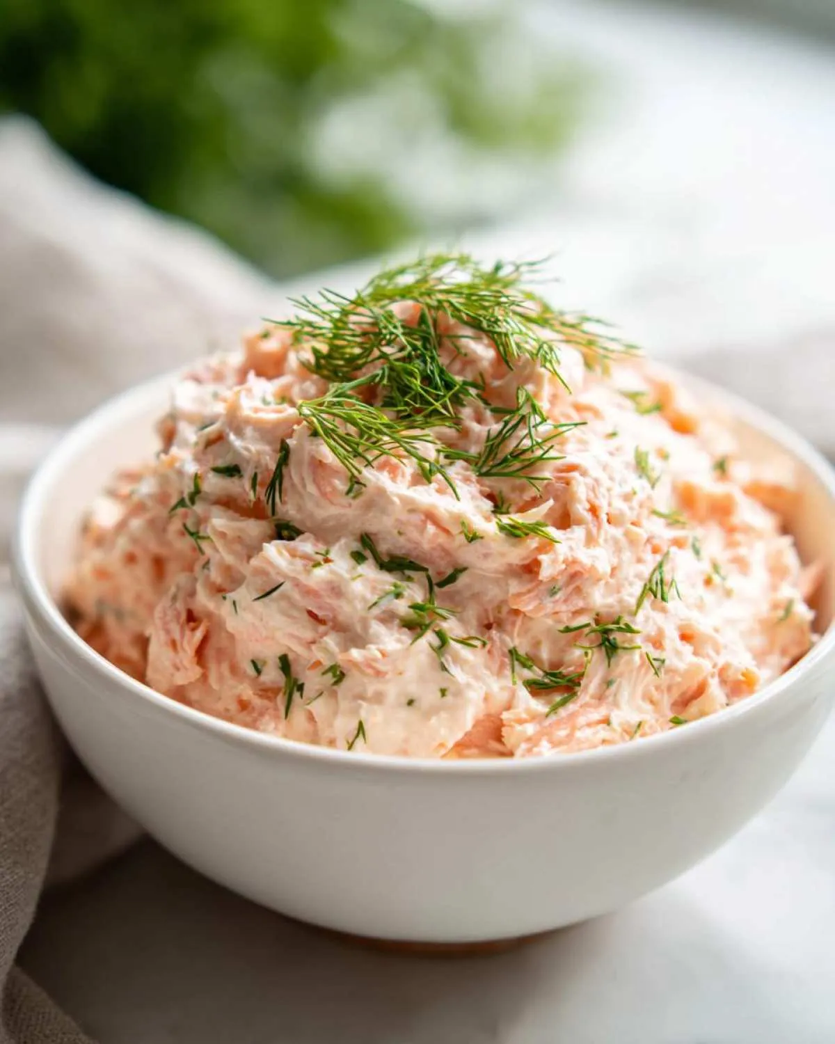 A close-up of creamy salmon dip mixed with herbs, topped generously with fresh dill sprigs.