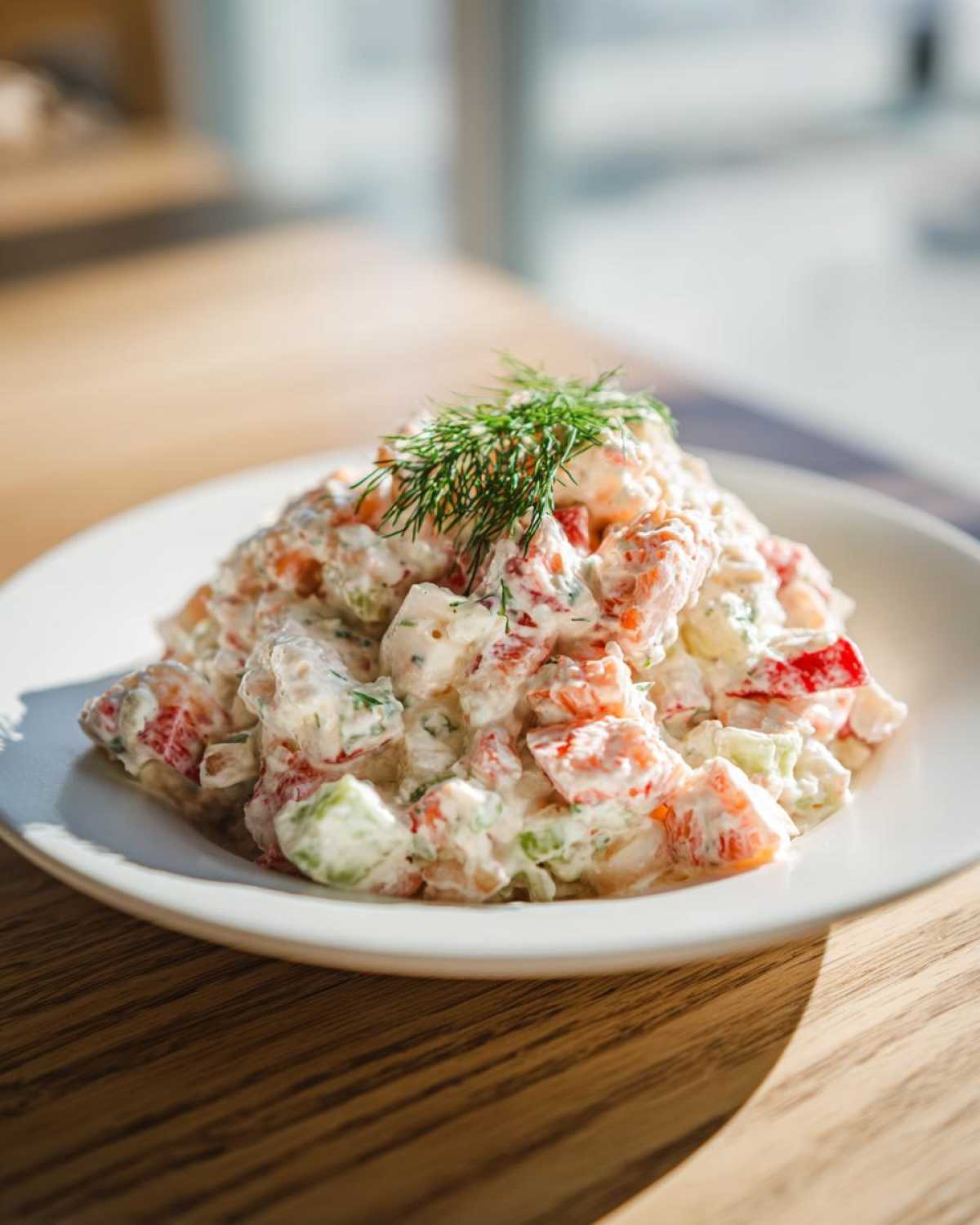 A mound of creamy seafood salad with visible chunks of seafood, red pepper, and celery, garnished with fresh dill.