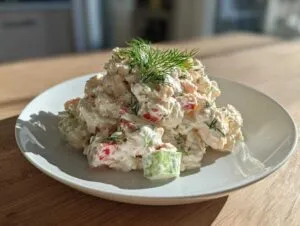 A mound of creamy seafood salad mixed with red peppers and cucumber, topped with fresh dill.