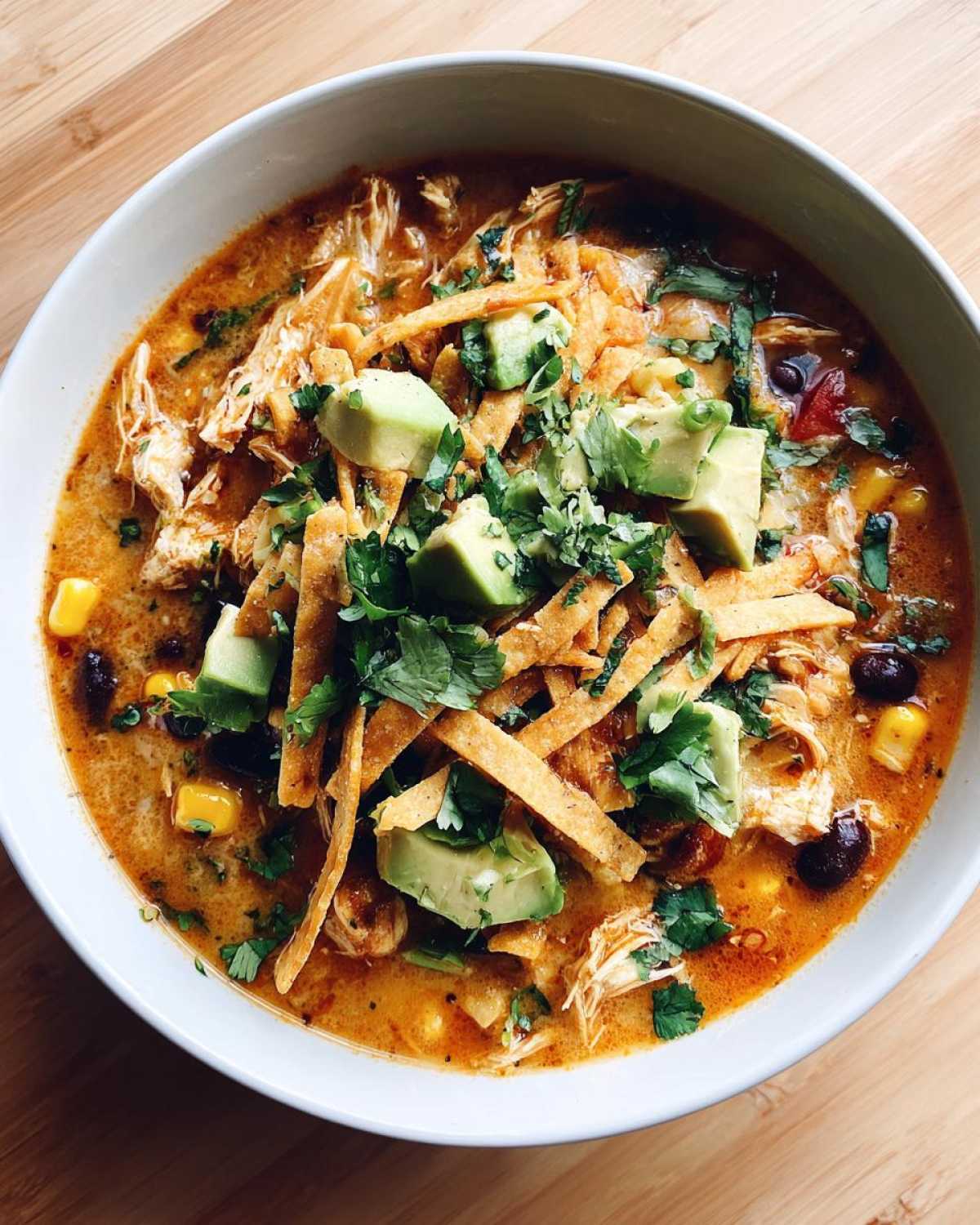 Overhead view of a creamy chicken tortilla soup recipe bowl, garnished with avocado, tortilla strips, and cilantro.