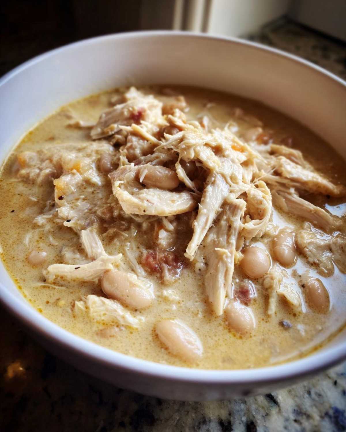 Close-up of a bowl filled with creamy white chicken chili, featuring shredded white chicken and white beans in a rich broth.