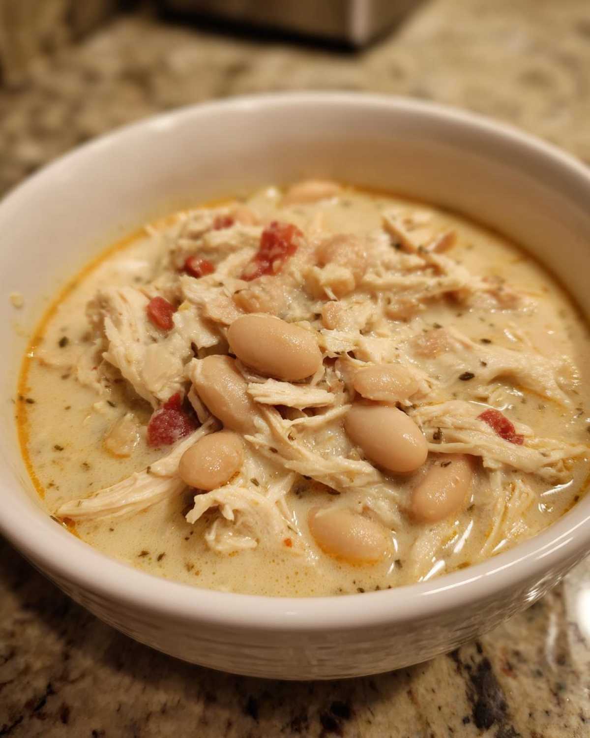 Close-up of a bowl of creamy white chicken chili featuring shredded white chicken and cannellini beans.