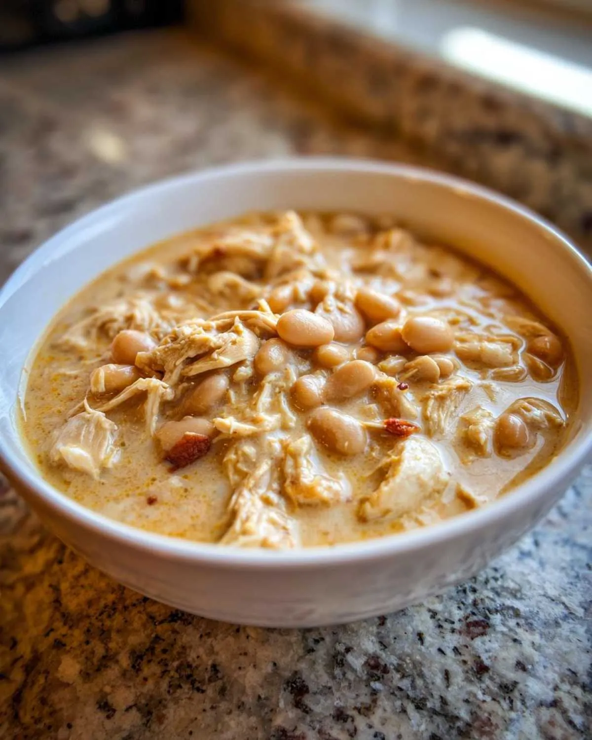 Close-up of a creamy bowl of white chicken chili featuring shredded white chicken and white beans.
