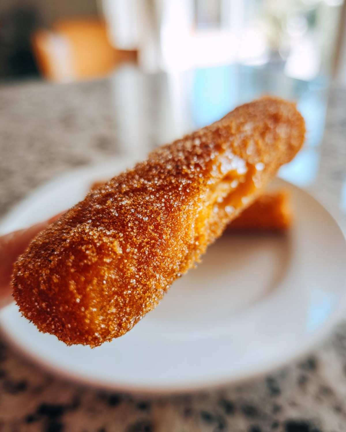 A close-up photo of a crispy, deep-fried item coated in cinnamon sugar, resembling a sweet corn dog.