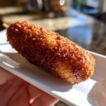Close-up of a perfectly crispy, golden brown homemade corn dogs on a white serving dish.