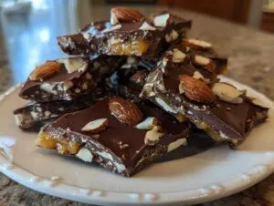 Stack of homemade almond chocolate toffee recipe pieces on a white plate, showing rich caramel and dark chocolate.