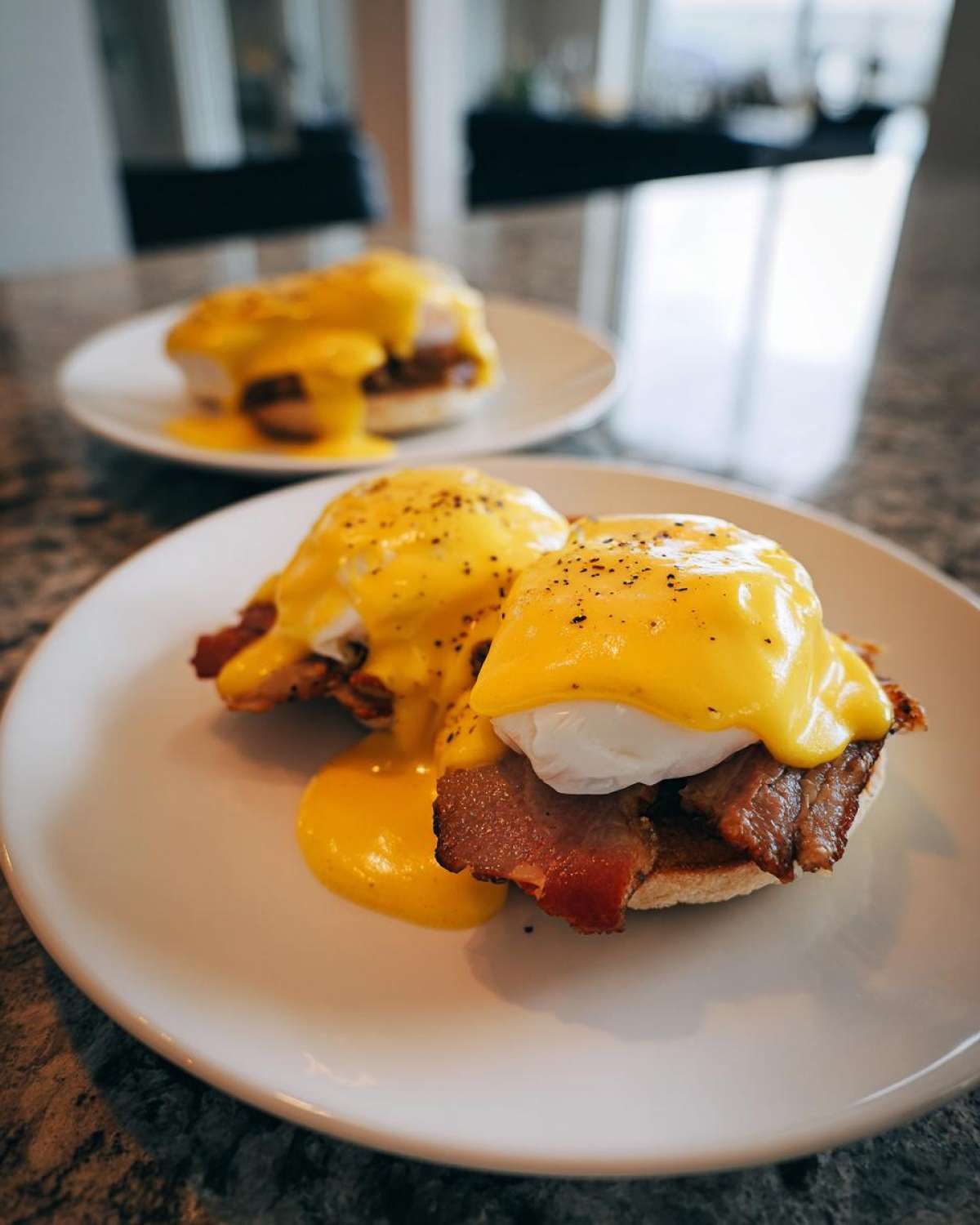 Close-up of two servings of eggs benedict topped with rich hollandaise sauce and cracked pepper.