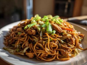 A close-up of a generous serving of homemade chicken chow mein recipe, topped with fresh green onions.