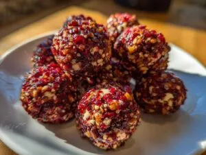 A pile of homemade goat cheese balls coated in a vibrant red, nutty, and fruity crust, served on a white plate.
