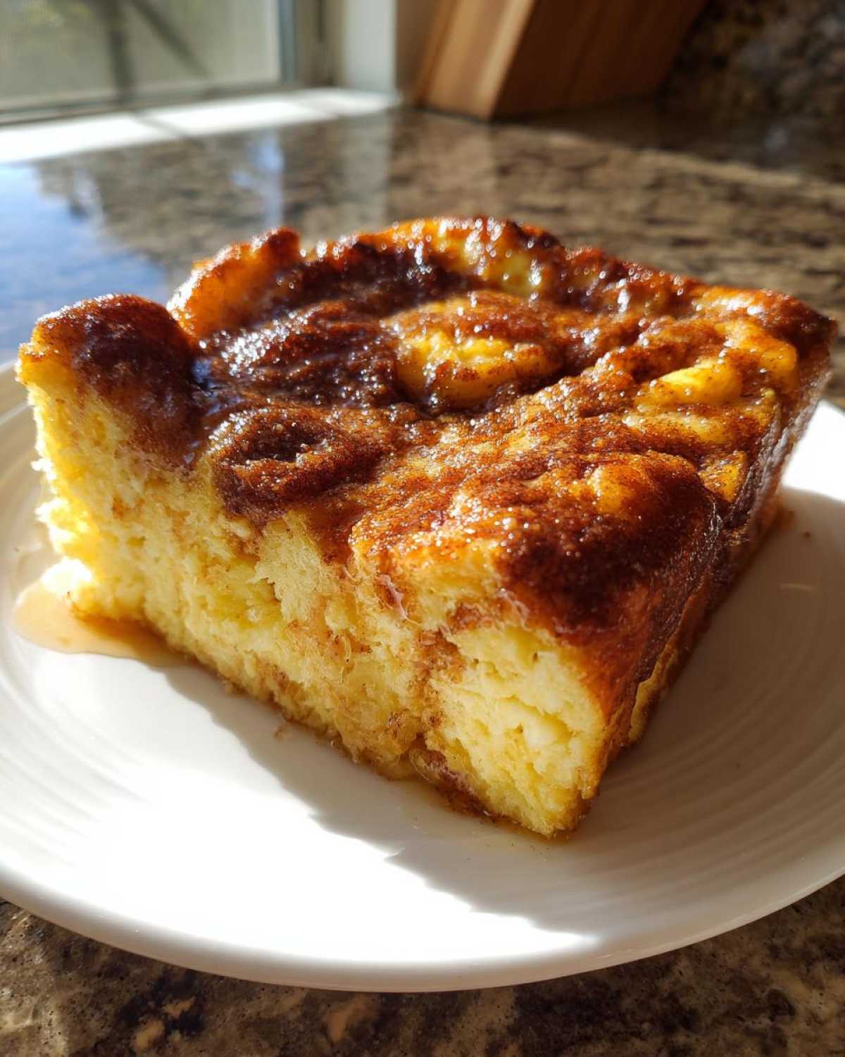 A square slice of fluffy baked French toast with a rich, caramelized cinnamon topping, served on a white plate.
