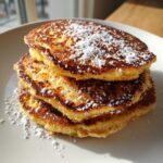 A close-up stack of three fluffy coconut flour pancakes dusted generously with white powdered sugar.