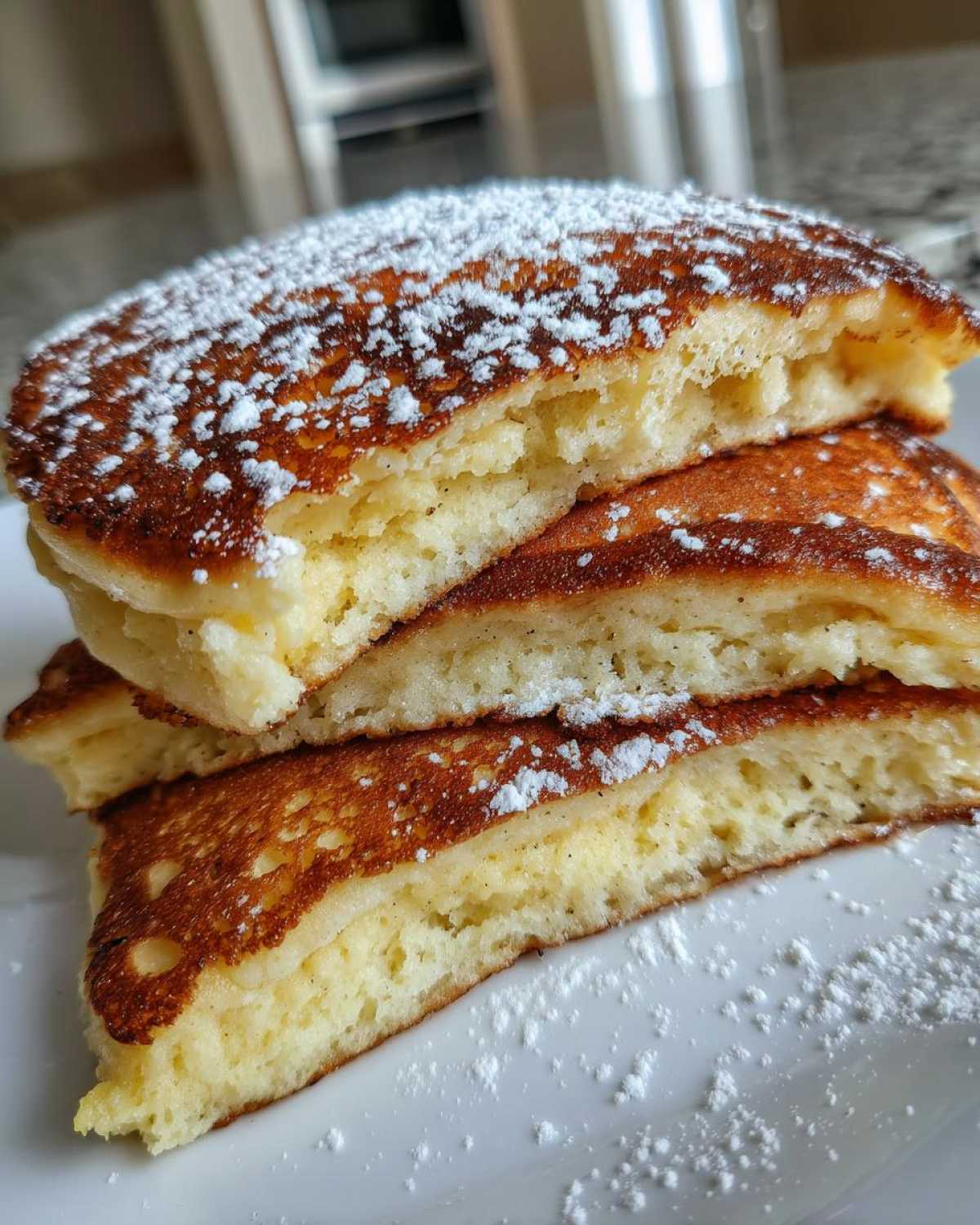 Close-up of three fluffy greek yogurt pancakes stacked and cut in half, dusted with powdered sugar.