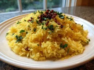 A mound of bright yellow mediterranean rice garnished with fresh parsley and toasted pine nuts on a white plate.