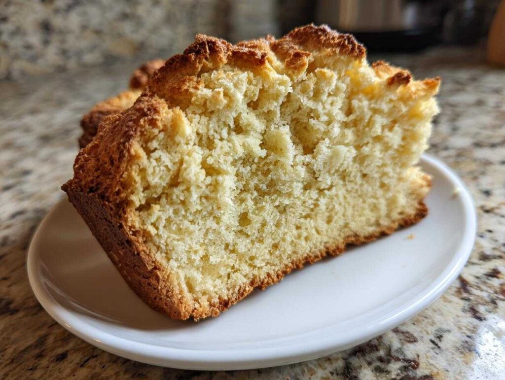 A thick slice of homemade soda bread showing its light, crumbly interior and golden-brown crust, served on a white plate.