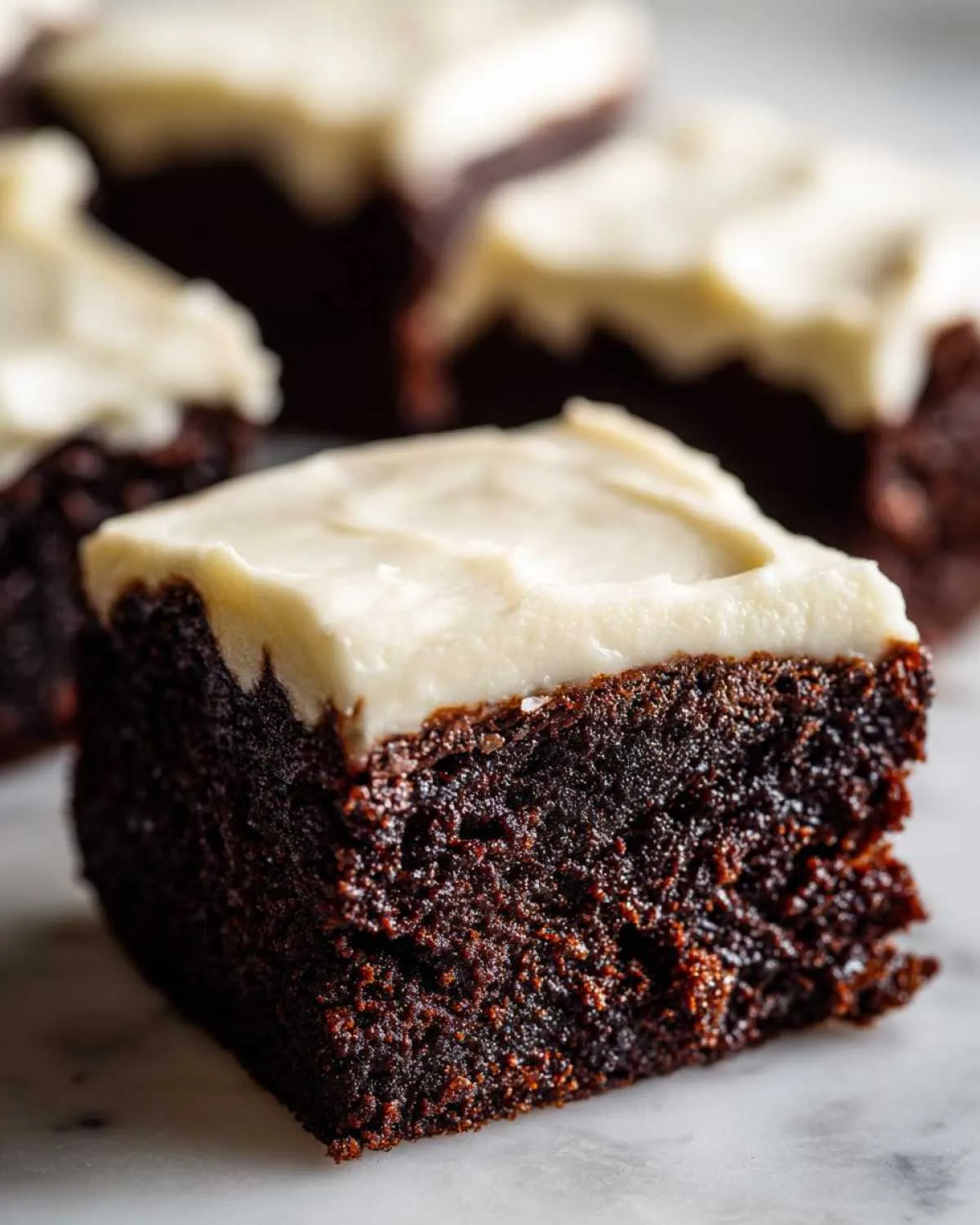 A moist, dark square of gingerbread brownies topped with thick, creamy white frosting.