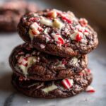 A stack of three fudgy chocolate peppermint cookies topped with melted white chocolate and crushed candy canes.