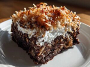 A moist slice of German Chocolate Poke Cake topped with whipped cream and toasted coconut flakes.